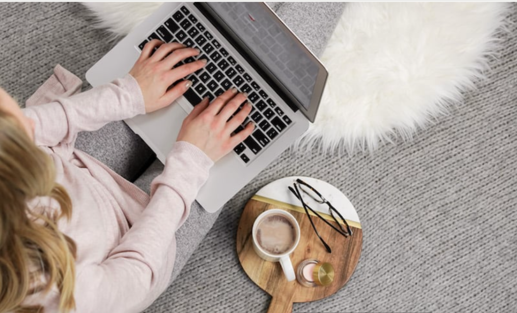 Top view of hands typing on a laptop with a coffee cup on a white desk
