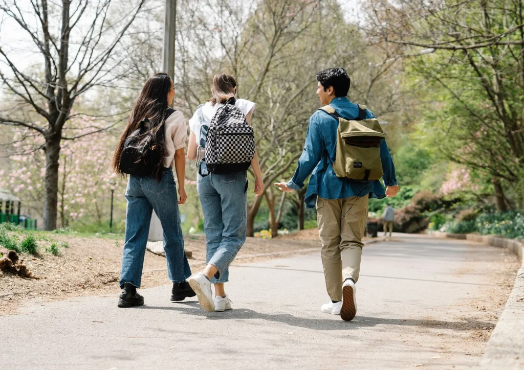 : College students walking on a campus pathway with backpacks in an outdoor setting