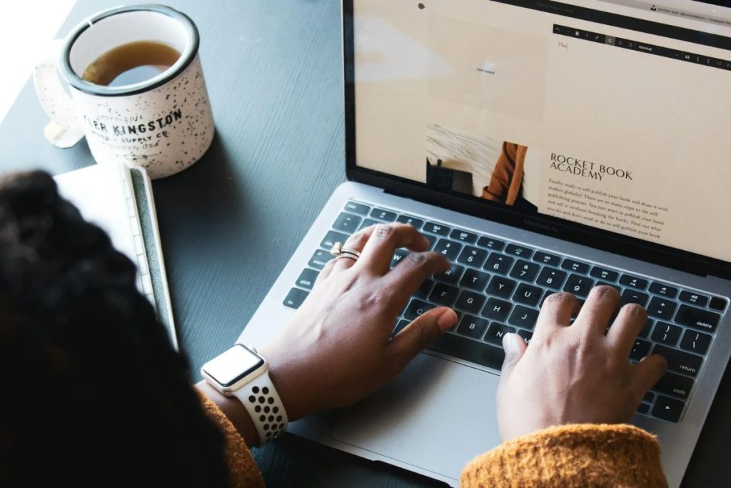 Person typing on a laptop with a coffee cup on the side representing freelance work
